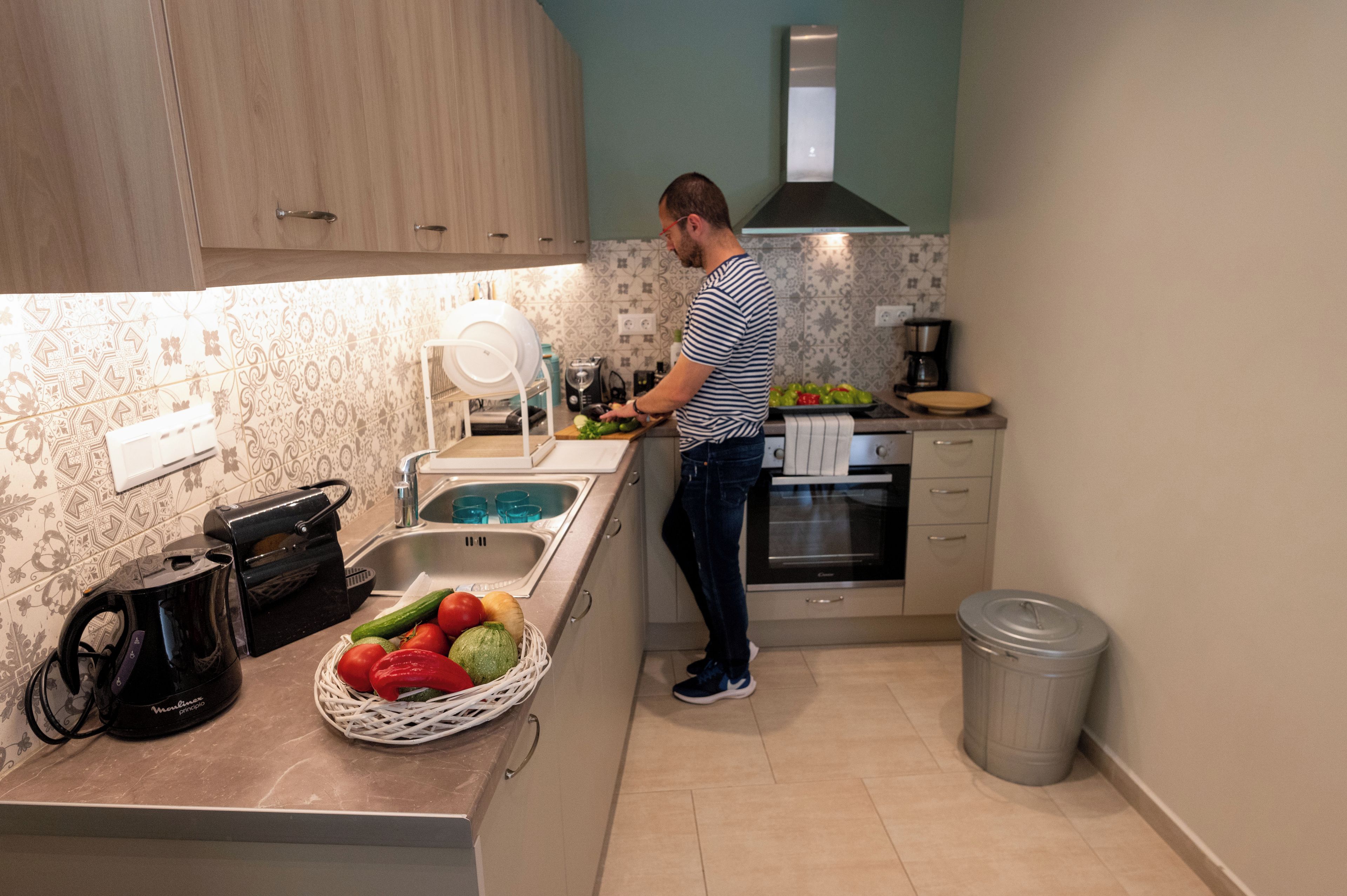 A kitchen with wooden cabinets, a sink, a coffee maker, and a trash can.