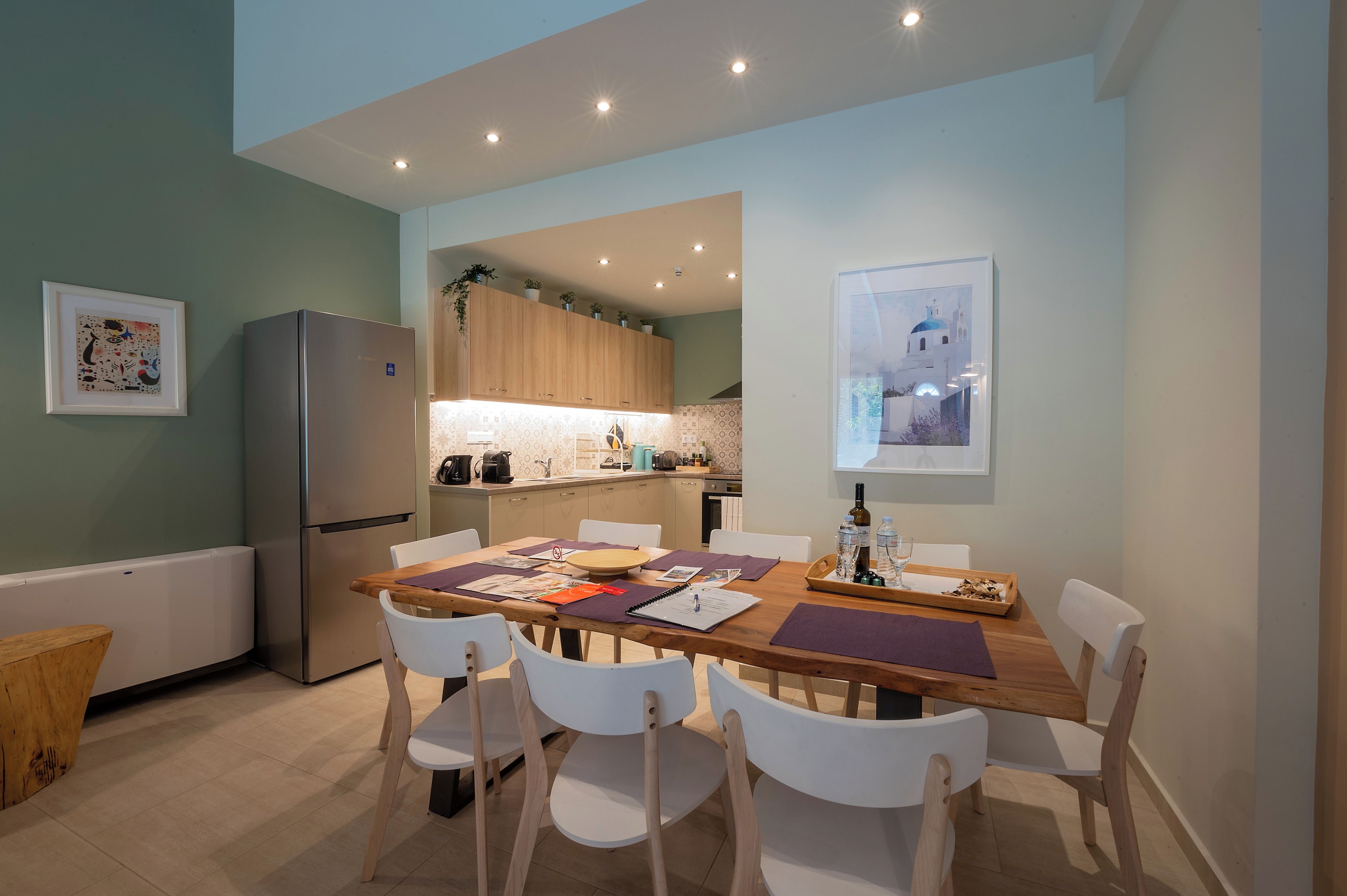 Une cuisine moderne avec des meubles en bois, un réfrigérateur en acier inoxydable et un coin repas comprenant une table en bois et des chaises blanches.