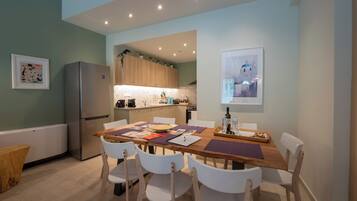 Une cuisine moderne avec des meubles en bois, un réfrigérateur en acier inoxydable et un coin repas comprenant une table en bois et des chaises blanches.