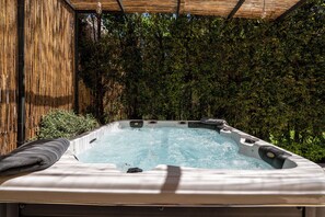 A hot tub with a wooden pergola overhead and a bamboo fence in the background.