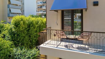 A balcony with wicker chairs and a table, surrounded by dense green foliage.