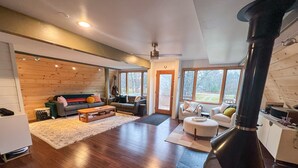 A modern living room with a fireplace, wooden flooring, and a sofa set. - Modern A-Frame on fenced, wooded Lot. Pet friendly! (East Tawas)