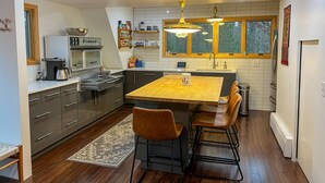 A modern kitchen with a central island, built-in appliances, and a large window providing natural light. - Modern A-Frame on fenced, wooded Lot. Pet friendly! (East Tawas)
