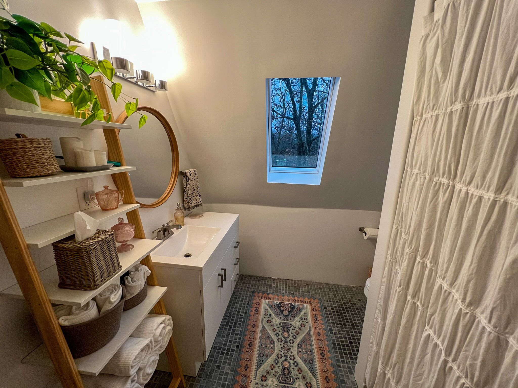 Een badkamer met een raam, planken met handdoeken en manden, een wastafel en een vloer met een patroon.