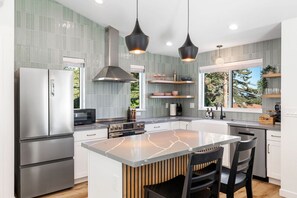 Une cuisine moderne dotée d’un îlot central, d’appareils électroménagers en acier inoxydable et de luminaires suspendus.
