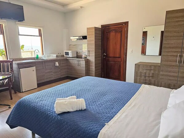 Een hotelkamer met een bed, een klein kitchenette, een houten garderobe en een raam met uitzicht.