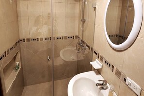 Een moderne badkamer met een douchecabine van glas, een witte wastafel en een ronde spiegel.