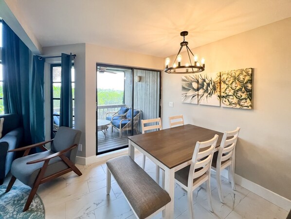 Un espace repas avec une table en bois et des chaises blanches, un banc et un lustre.