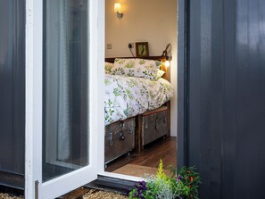 Une chambre à coucher avec un lit, une lampe fixée au mur, un tableau encadré et une valise sous le lit.