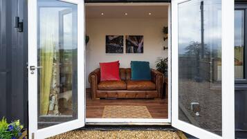 An open door to a room with a brown leather sofa, two cushions, and a small rug.