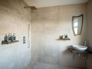 Une salle de bain moderne équipée d’une douche, d’un lavabo et de deux étagères où sont rangés les produits de toilette.