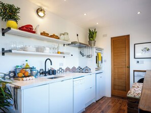 Une cuisine de taille réduite avec des meubles blancs, un évier et un plan de travail sur lequel sont disposés divers objets.