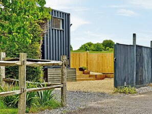 Une clôture en bois rustique, un bâtiment en métal et un chemin de gravier.