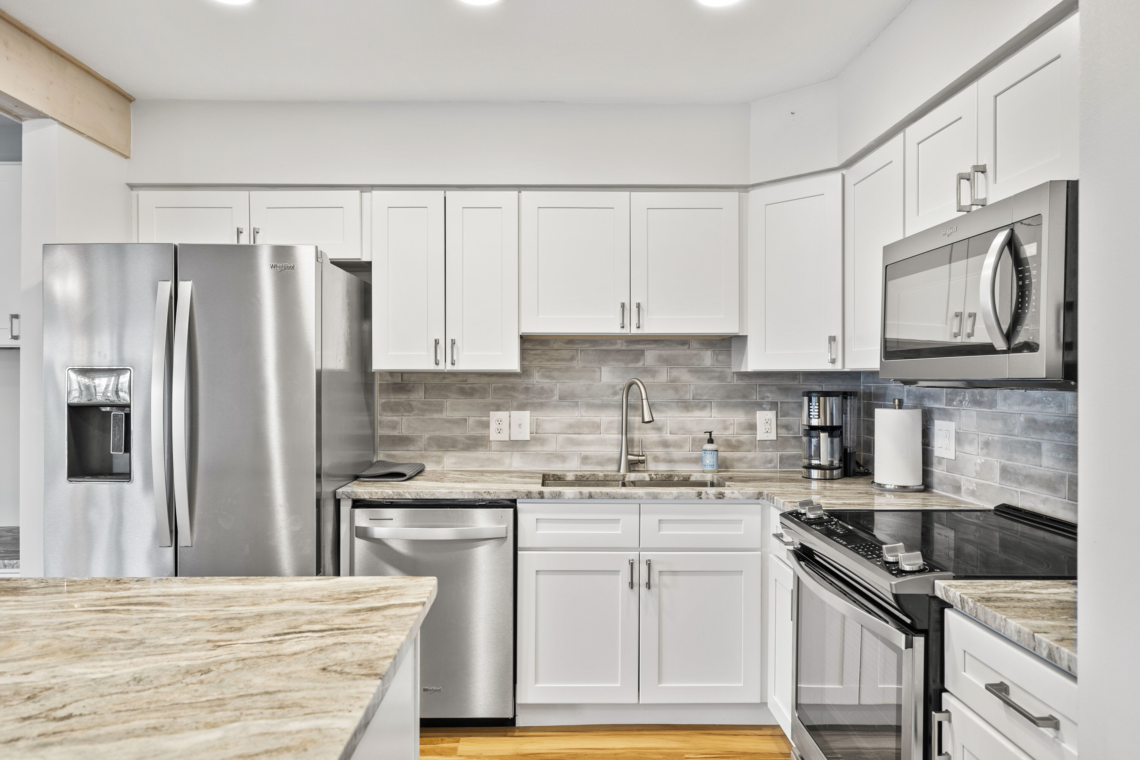 A modern kitchen with white cabinets, stainless steel appliances, a marble countertop, and a built-in oven.