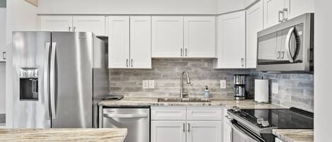 A modern kitchen with white cabinets, stainless steel appliances, a marble countertop, and a built-in oven.