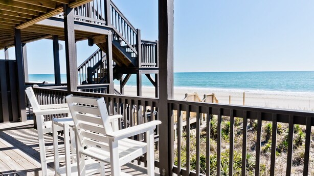 Terraza de madera con sillas blancas con vista a la playa.