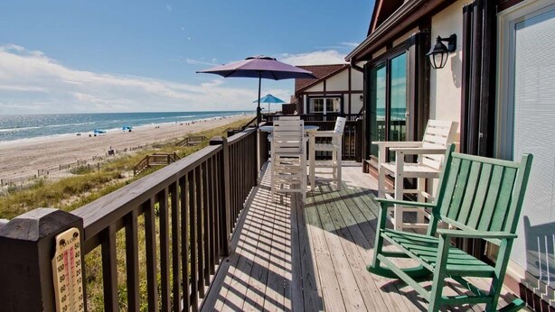 A wooden deck with a view of the beach, outdoor seating, and a blue umbrella. - Ocean Reef 4-B2, Oceanfront Condo in Emerald Isle, NC! (Emerald Isle)