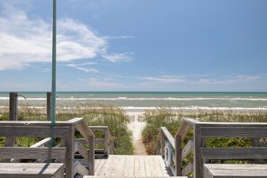A wooden boardwalk leading to a beach with a clear view of the ocean.