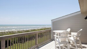 A wooden deck with a view of the ocean, white chairs, and a small table. - Ocean Terrace #2, Oceanfront Condo in Pine Knoll Shores, NC! (Pine Knoll Shores)
