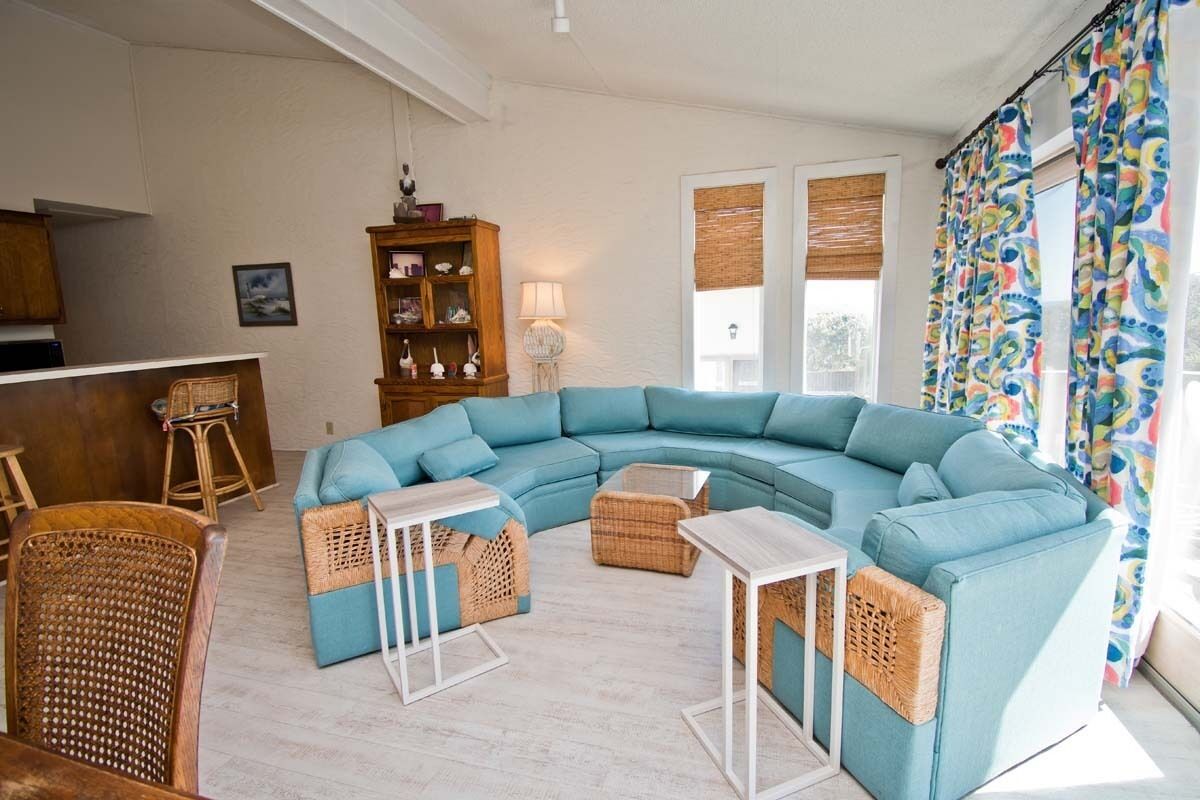 A living room with a teal sectional sofa, wicker ottomans, and a white coffee table.