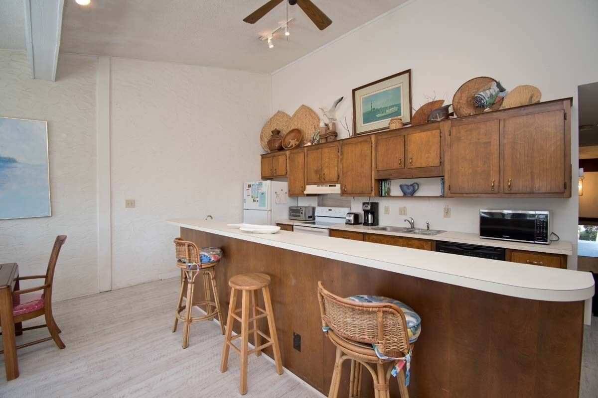 A kitchen with wooden cabinets, a white countertop, and bar stools.