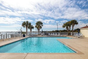 A swimming pool with a white fence, palm trees, and a view of the water. - Olde Towne Yacht Club 215, Soundfront Condo in Beaufort, NC! (Beaufort)