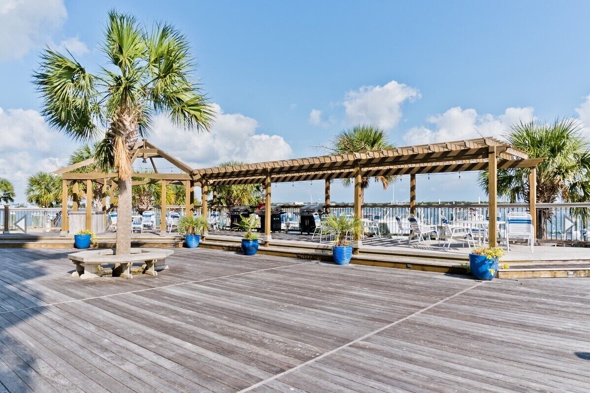 A wooden deck with a pergola, seating, and potted plants.