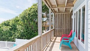 Une terrasse en bois avec une rambarde, deux chaises et une vue sur les arbres.