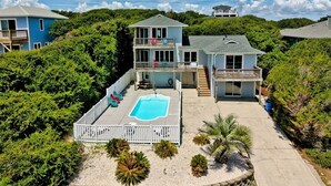 Une maison à deux étages avec une piscine, entourée d’une végétation luxuriante et sous un ciel dégagé.
