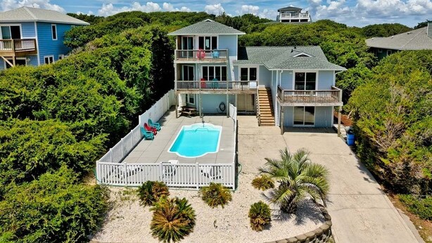 Une maison à deux étages avec une piscine, entourée d’une végétation luxuriante et sous un ciel dégagé.