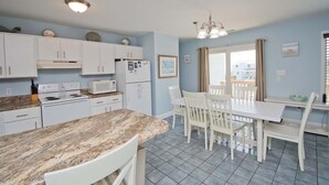 Une cuisine avec des meubles blancs, un plan de travail en granit, une table à manger avec des chaises et une fenêtre avec des rideaux.