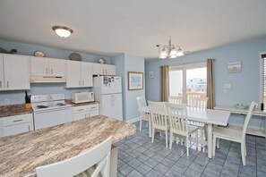 A kitchen with white cabinets, a granite countertop, a dining table with chairs, and a window with curtains. - Page One, Almost Oceanfront House in Emerald Isle, NC! (Emerald Isle)