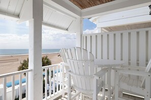 A white wooden deck with a table and chairs overlooking a beach.