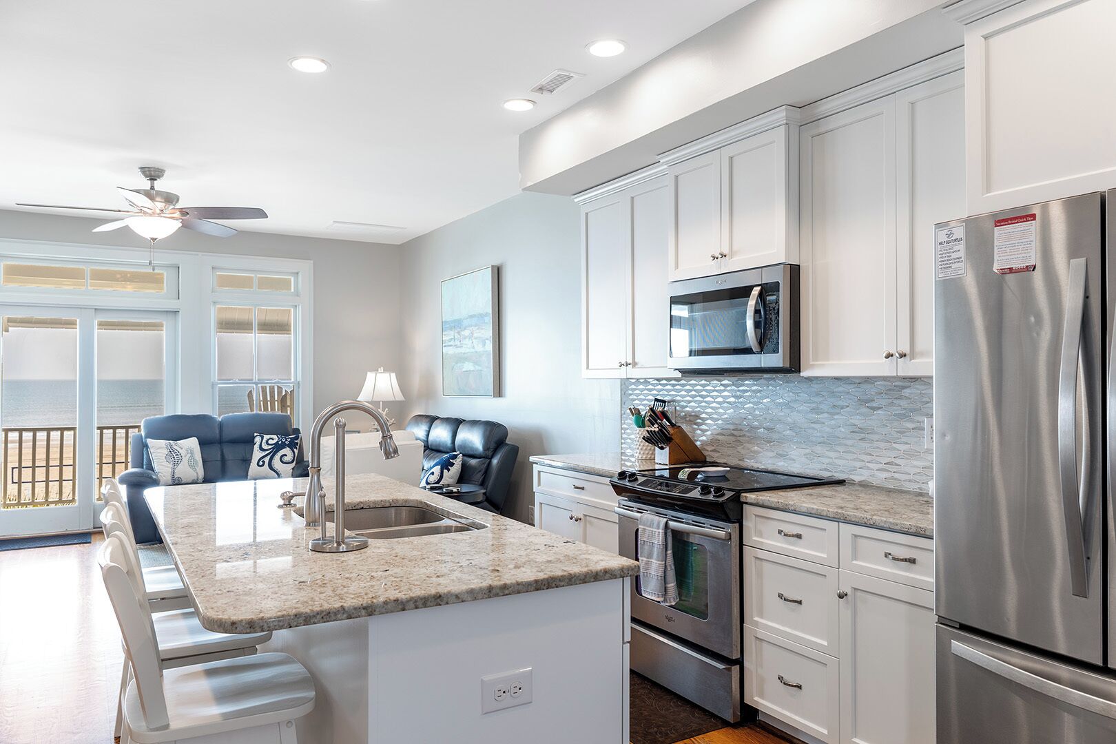 A modern kitchen with white cabinets, stainless steel appliances, a granite countertop, and a view to the outside.