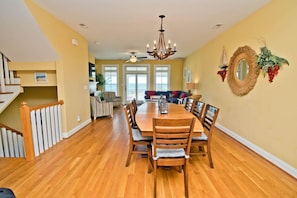 A dining area with a wooden table and chairs, a chandelier, and a view of the outdoors through large windows.