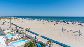 A beach with a volleyball net, a pool area, and beach umbrellas. - Palm Cottage III At The Grove, Oceanfront House in Atlantic Beach, NC! (Atlantic Beach)