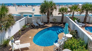 A pool area with a wooden deck, lounge chairs, and a view of the beach. - Palm Cottage III At The Grove, Oceanfront House in Atlantic Beach, NC! (Atlantic Beach)