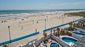 Une vue sur la plage avec un espace piscine, comprenant un filet de volley-ball et des chaises longues.
