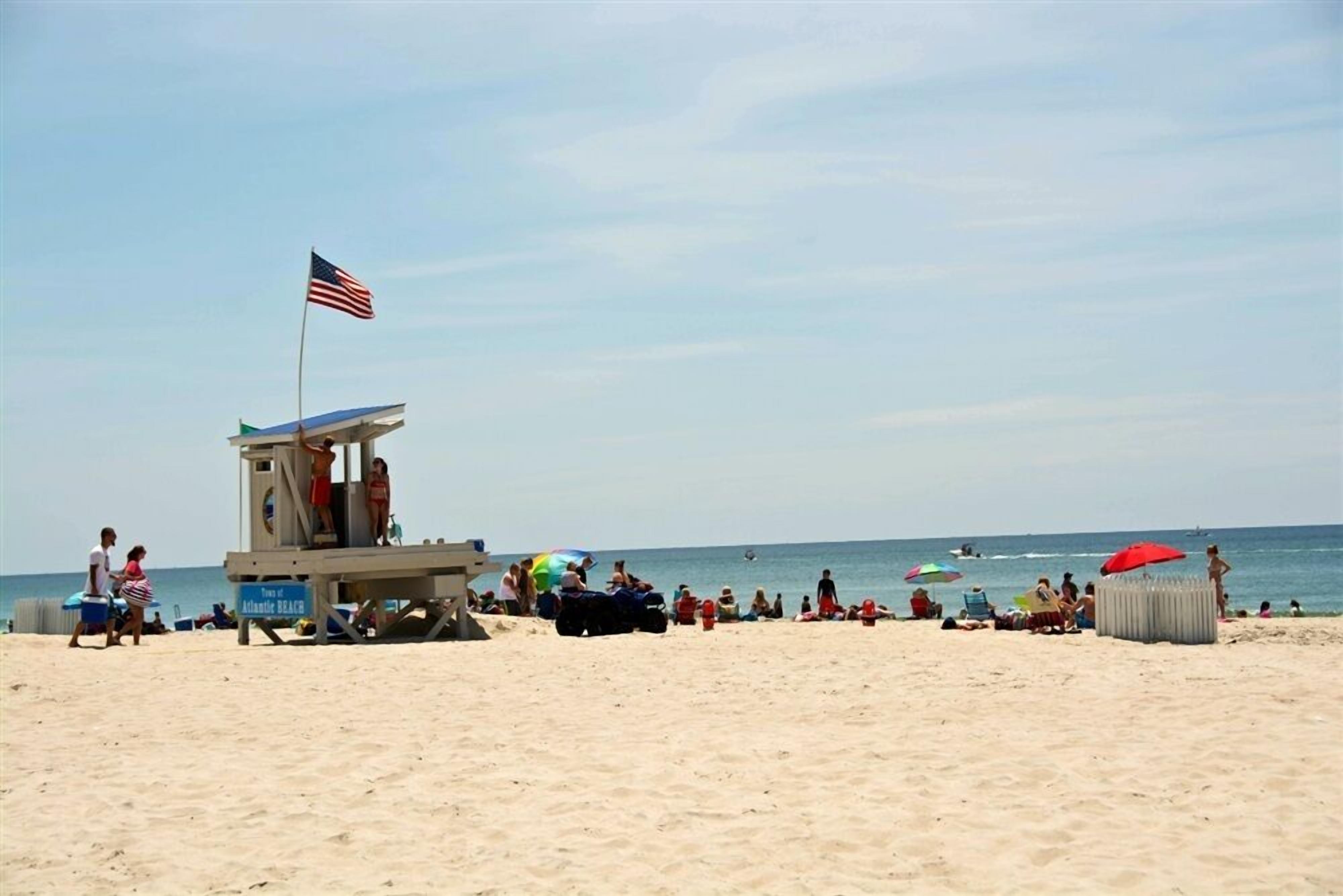 A lifeguard tower with an American flag, beach umbrellas, and people on the sand.