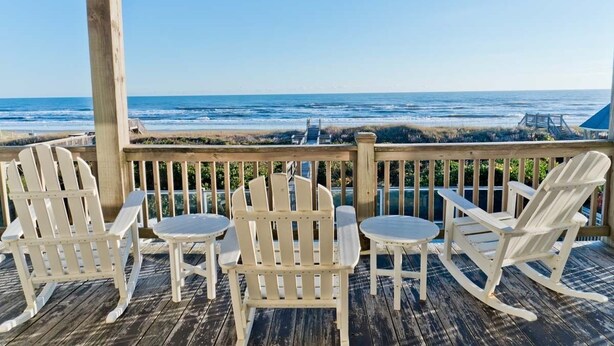 Une terrasse en bois, agrémentée de fauteuils Adirondack et de petites tables, avec vue sur l’océan.