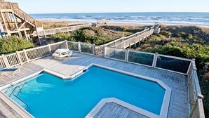 Une terrasse en bois avec une piscine, un escalier en bois menant à la plage et une vue sur l’océan.