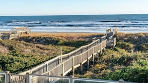 Une promenade en bois mène à une plage, et une structure en bois se trouve sur la gauche.