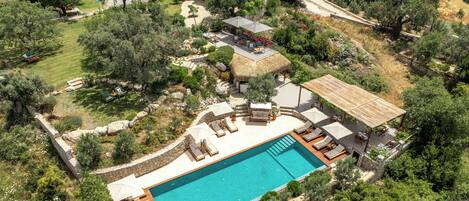 An aerial view of a residential property with a swimming pool, outdoor seating, and a garden.