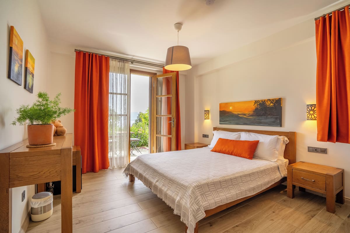 A bedroom with a bed, wooden nightstands, a bedside table with a plant, and a view through a glass door.