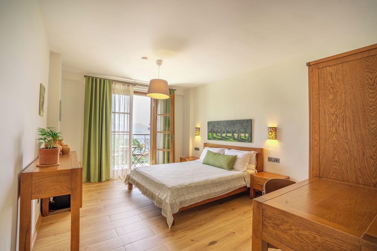 A bedroom with a wooden bed, a nightstand, a desk, and a balcony with green curtains.