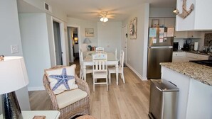 A modern kitchen with white cabinetry, a stainless steel refrigerator, and a granite countertop. - Pebble Beach A-107, Oceanfront Condo in Emerald Isle, NC! (Emerald Isle)