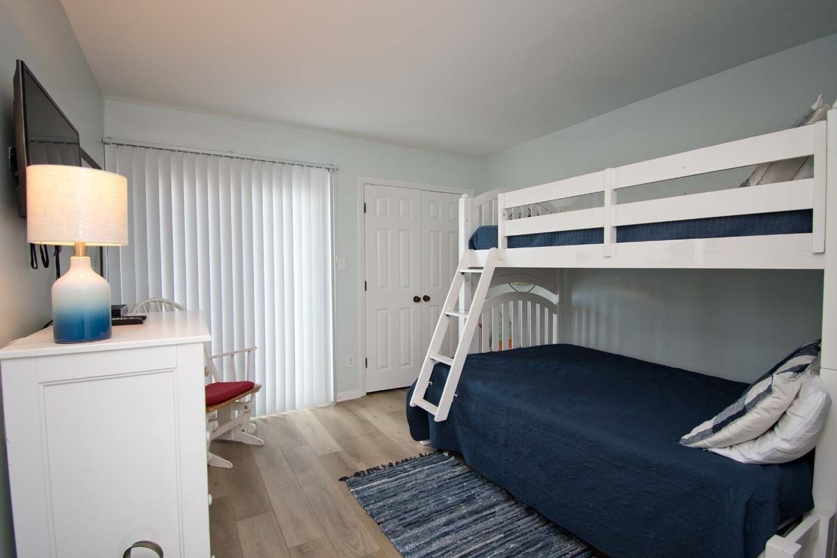 A bedroom with bunk beds, a desk with a lamp, a chair, and a door.