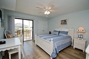 Un dormitorio con cama, escritorio, silla, ventilador de techo y vistas al exterior.