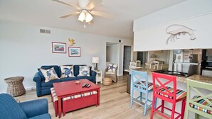 A living room with a blue sofa, red coffee table, and colorful chairs. - Pebble Beach A-107, Oceanfront Condo in Emerald Isle, NC! (Emerald Isle)