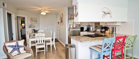 A compact kitchen with white cabinetry, a stainless steel refrigerator, and a small island with colorful chairs.